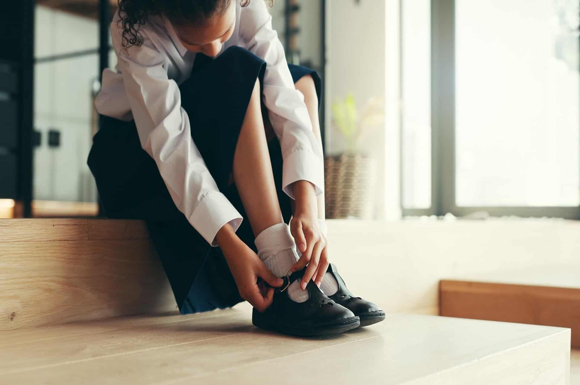 A girl putting on school shoes.